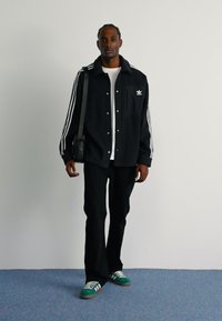 Černá oversized košilová bunda s bílými pruhy, spárovaná s bílým tričkem a černými kalhotami. Zeleno-bílé pruhované tenisky.