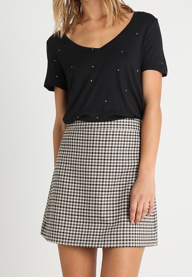 Femme portant un haut noir à manches courtes avec de petits pois et une jupe taille haute à carreaux noirs et blancs.