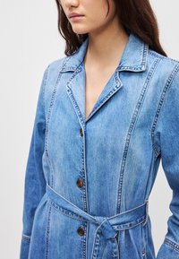 Δερμάτινο παλτό σε ανοιχτό μπλε με μακριά μανίκια, γιακά με εγκοπές, μπροστινά κουμπιά και ζώνη στη μέση, με κάθετες ραφές.