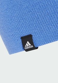 Blue knit beanie with textured fabric, featuring a black Adidas logo tag on the side. The design is simple and functional.