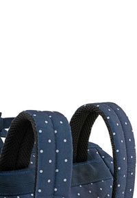 Mochila azul marino con lunares blancos, con correas de malla negra acolchadas y un exterior de tela resistente.