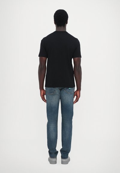 T-shirt en coton noir associé à un jean en denim bleu, avec une coupe droite et un design classique à cinq poches. Des baskets grises complètent le look.