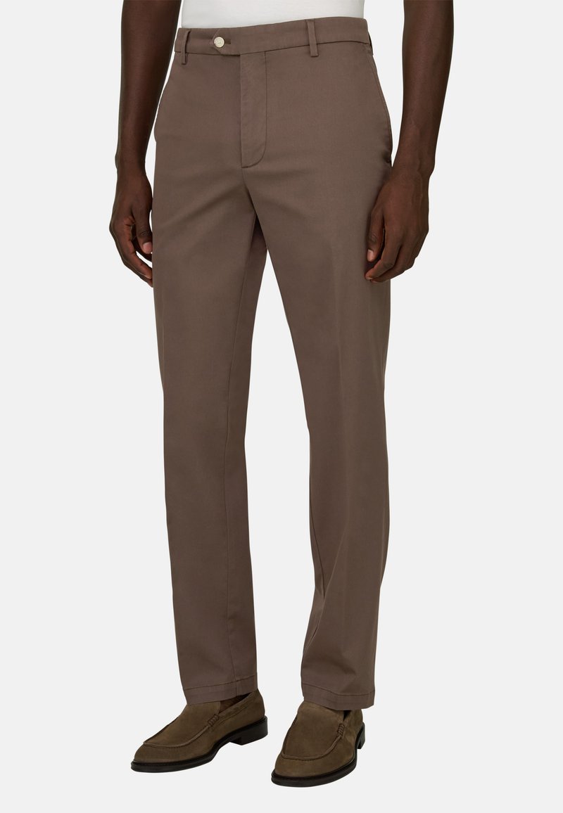 Homme portant un pantalon droit marron et des mocassins en daim marron, debout devant un fond blanc uni.