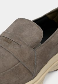 Chaussure à enfiler en suède marron avec semelle beige et panneau latéral élastique pour un enfilage facile, marquée "GLOBE" sur la bride traversant le dessus.