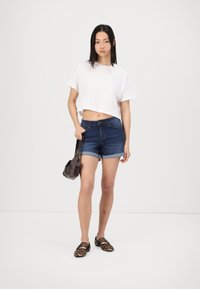 T-shirt branca cortada, calções de ganga azul escuro com as bainhas dobradas, sapatos planos de estampa de leopardo e uma pequena bolsa cruzada castanha.