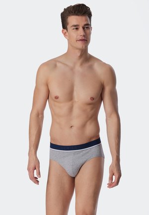 Graue Baumwollunterhosen mit einem marineblauen Bund, der weiße Akzente und Markenlogo aufweist. Das Modell steht mit neutralem Gesichtsausdruck und natürlicher Haltung.
