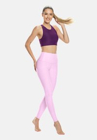 Fialová sportovní podprsenka a světlé růžové legíny s vysokým pasem, obojí vyrobené z pružné tkaniny. Vyznačují se hladkým povrchem a přiléhavým střihem.