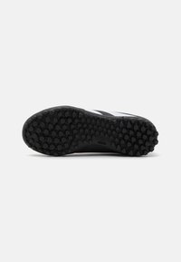Suela de zapato atlético negra con un patrón texturizado de espigas hexagonales para proporcionar agarre. Presenta un borde negro suave con detalles blancos cerca del talón.