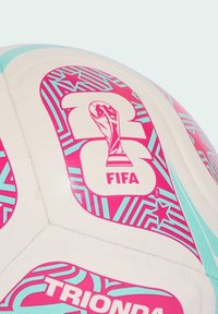 Nogometna lopta s bijelom sintetičkom površinom. Osvijetljeni ružičasti i tirkizni geometrijski uzorci, FIFA logo i dizajn trofeja istaknuti su.
