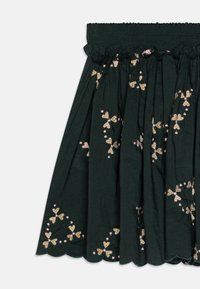 Grønn brodert skjørt med smocket midje, med blomsterdesign i rosa og gull, og en bølget kant. Lett stoff.