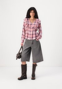 Pink plaid blouse with ruffled neckline, paired with gray wide-leg shorts and knee-high brown boots, holding a small brown bag.