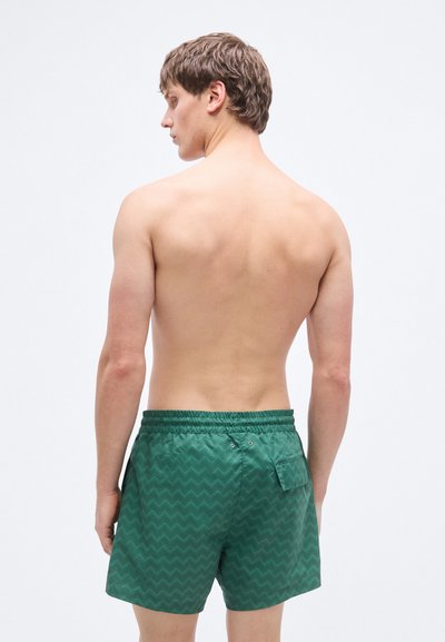 Πράσινο μαγιό με σχέδιο ζικ-ζακ, κατασκευασμένο από ελαφρύ υλικό. Διαθέτει ελαστική μέση και πίσω τσέπη με κούμπωμα με πάτημα.