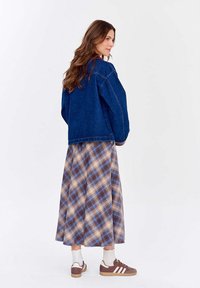 Džínsová bunda s volným střihem, doplněná dlouhou károvanou sukní s modrými, hnědými a krémovými vzory. Součástí jsou i neformální boty.