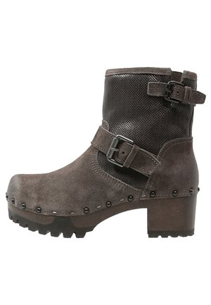 Bottine en daim marron à bout rond, panneau en maille noire, boucle latérale et clous décoratifs le long de la base ; talon épais et semelle texturée.