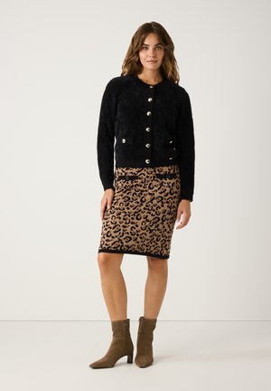 Schwarze, flauschige Strickjacke mit großen silbernen Knöpfen, kombiniert mit einem Bleistiftrock im Leopardenmuster in Beige und Schwarz sowie taupefarbenen Knöchelstiefeln.