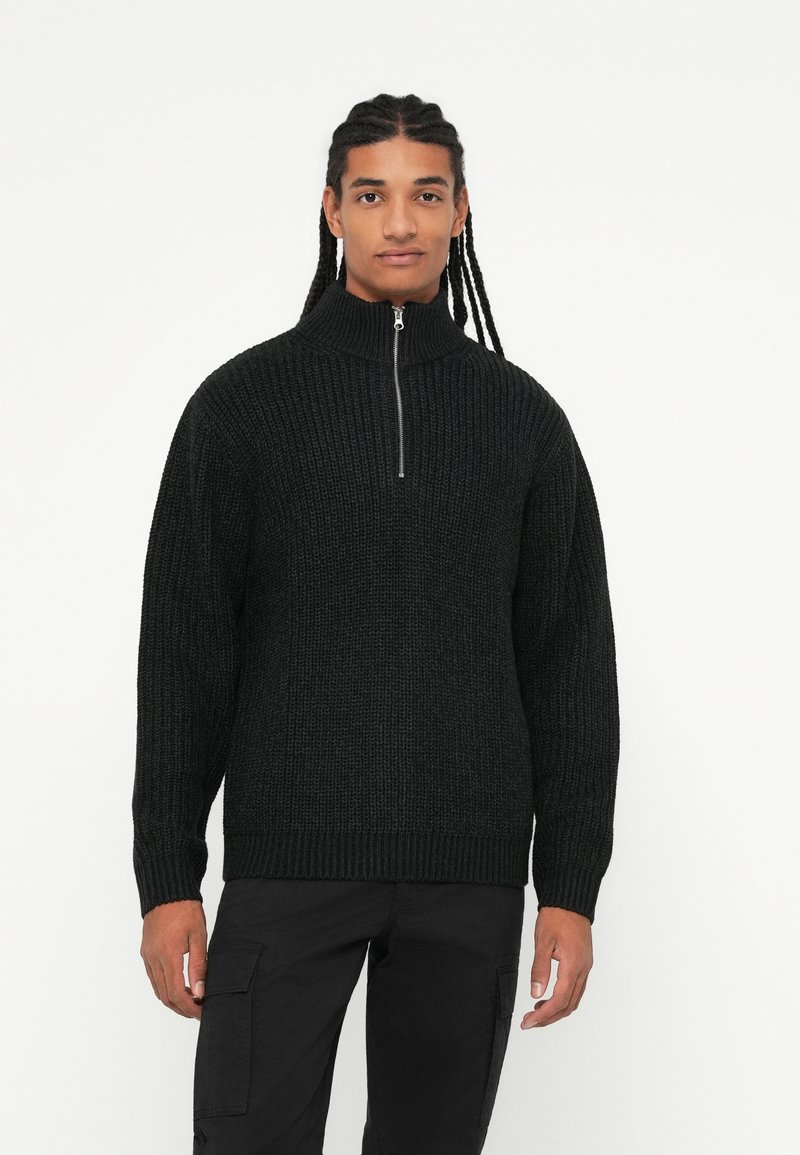 Maglione nero lavorato a maglia con zip e colletto alto, texture a coste e ampi polsini, abbinato a pantaloni cargo neri.