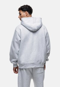 Felpa grigia con cappuccio, dal taglio rilassato, texture morbida e polsini a coste. Caratterizzata da un grande cappuccio e design minimalista.