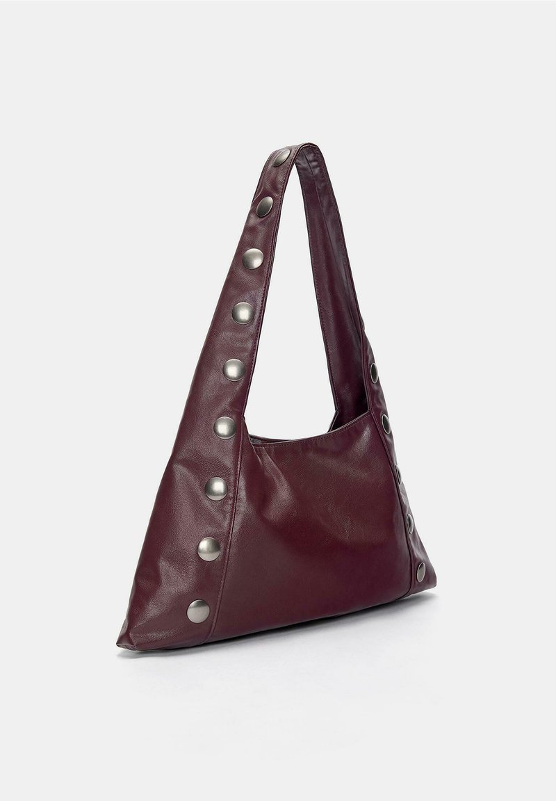 Bolso de hombro de cuero burdeos oscuro con una correa ancha y grandes tachuelas plateadas en los bordes, sobre un fondo claro y liso.