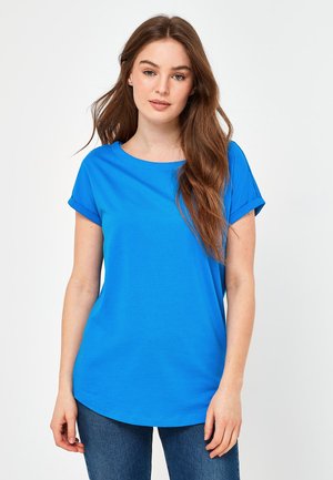 Blå kortärmad t-shirt med rund hals, tillverkad av ett mjukt tyg, med rullade ärmar och en avslappnad passform, kombinerad med jeans.