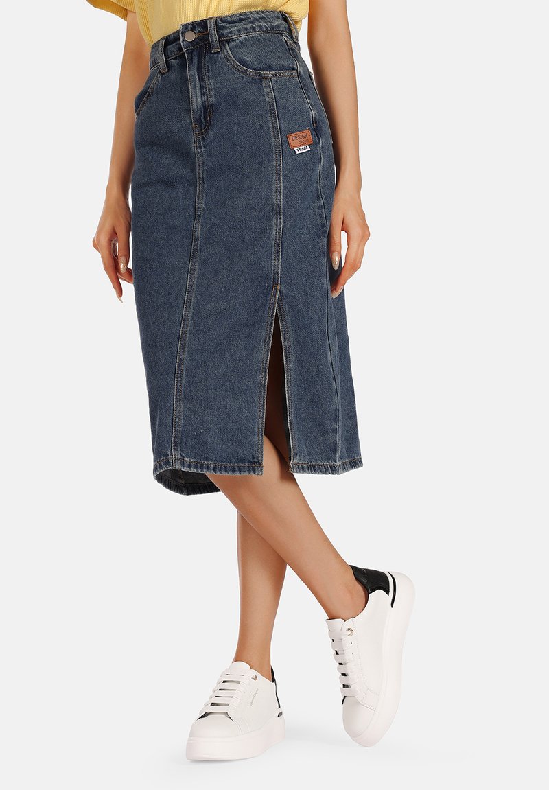 Gonna midi in denim con spacco anteriore, tasche a filetto, lavaggio azzurro chiaro e un patch con il marchio. Abbinata a sneakers bianche con accenti neri.