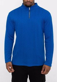 Pull bleu à col zippé avec un motif de tricot texturé, manches longues et design ajusté. Le matériau semble doux et chaud.