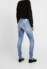 Jasnoniebieskie skinny jeans z przetarciem, subtelnym wyczerpaniem, dwiema tylkimi kieszeniami oraz białą metką na pasku. Połączone z czarnymi balerinami.