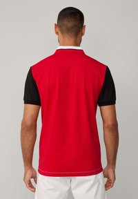 Camisa polo roja con mangas negras, que presenta un cuello clásico y detalles de costura. Tejido suave con una silueta deportiva.