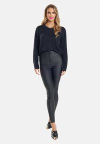 Schwarzer, flauschiger Pullover kombiniert mit hoch taillierten, schwarzen, eng anliegenden Lederhosen und schwarzen Schuhen mit goldenen Akzenten. Schlanke Passform, lange Ärmel.