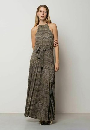 Donna in piedi che indossa un vestito lungo senza maniche con collo all'americana, fantasia, cintura annodata in vita e scarpe con punta appuntita.