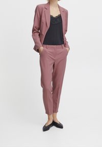 Rose-colored blazer and matching tailored trousers paired with a black lace-trimmed camisole and black flats. Smooth, structured fabric.