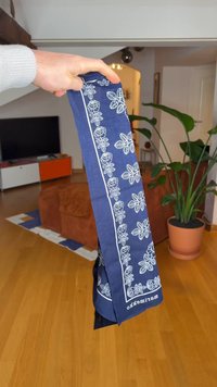 Lenço azul marinho com padrões florais brancos e bordas. Feito de tecido leve, tem forma retangular com bordas acabadas.