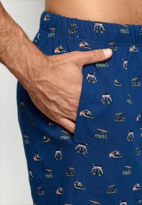 Bermude de culoare bleumarin cu un model repetat de mașini echipate cu plăci de surf micuțe. Confectionate dintr-un material moale, cu un tiv elastic.