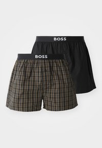 Zwei Paare Boxer-Shorts: eine in solidem Schwarz, die andere im karierter Muster in Braun und Marineblau. Beide haben einen elastischen Bund mit Markenlogo.
