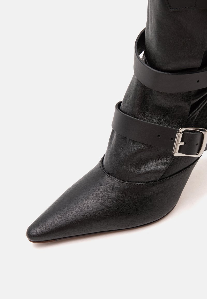 Black pointed-toe leather boot with two black straps and a silver buckle around the ankle against a white background.