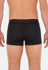 Boxer di cotone neri con una cintura logo rossa, design aderente e texture liscia. Taglio a metà coscia, vista posteriore.