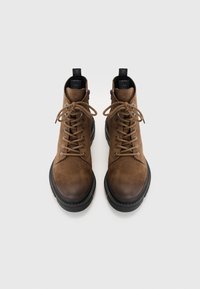 Brown suede ankle boots with a rounded toe, black rubber sole, and lace-up design. Features metal eyelets and pull tabs at the heel.