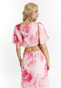 Completo a due pezzi composto da una maglietta corta a maniche corte e una lunga gonna coordinata. Realizzato in tessuto leggero con un motivo ad acquerello rosa.
