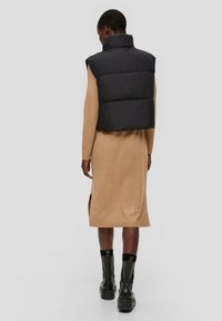 Zwarte donsvest met hoge kraag over een beige jurk tot de knie met zijsplitten en zwarte enkelboots met dikke zolen.