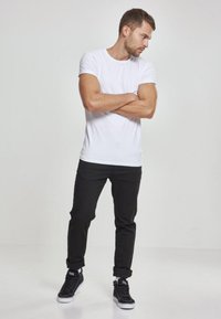 Tricou alb cu mânecă scurtă asociat cu blugi negri slim-fit și adidași negri. Ținuta are un design simplu și linii curate.