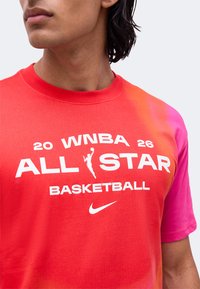 Άτομο που φορά μπλουζάκι μπάσκετ WNBA All Star με κόκκινο και ροζ βαθμωτό σχέδιο, λευκό κείμενο και λογότυπο Nike στο στήθος.