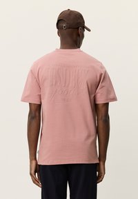 Κοντομάνικο T-shirt σε σκόπιμο ροζ χρώμα με ανάγλυφο λογότυπο στο πίσω μέρος, κατασκευασμένο από απαλό βαμβακερό υλικό. Απλό σχέδιο, casual εφαρμογή.