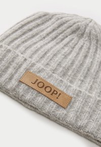 Hallus halli kudum müts, millel on ribatud tekstuur ja nahast märgiga, millel on pruunis kirjas "JOOP!". Kompaktne kuju, et sobituda tihedalt.