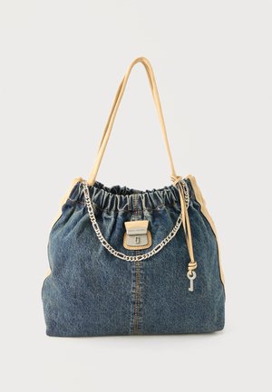 Borsa in denim con rifiniture in pelle color cuoio, tracolle, dettaglio con catena argentata e un piccolo ciondolo a forma di chiave appeso, su uno sfondo semplice.