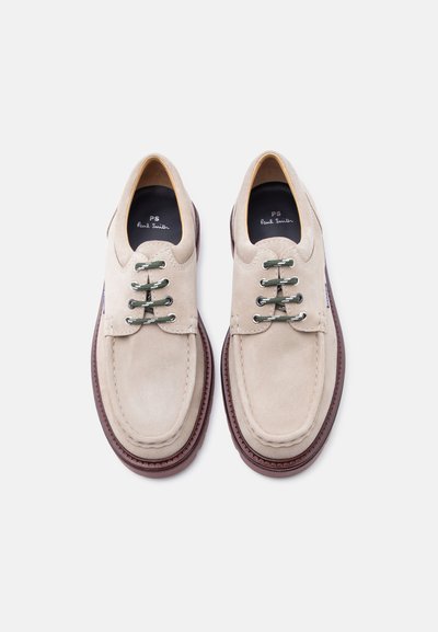 Chaussures en daim beige clair à lacets avec des lacets vert foncé et des semelles marron, vues de dessus sur un fond blanc.