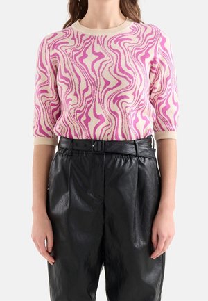 Woman wearing a pink and cream wavy patterned knit top with elbow-length sleeves and high-waisted black belted faux leather pants.