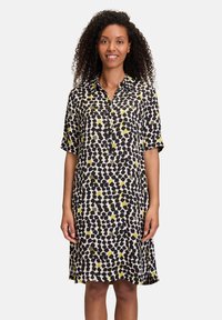 Abito camicia a maniche corte con motivo nero e giallo, con chiusura frontale a bottoni e vestibilità comoda. Il tessuto sembra leggero e morbido.