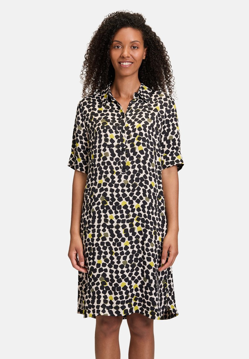 Schwarz-gelb gemustertes Hemdkleid mit kurzen Ärmeln, knöpfbarem Vorderteil und lockerer Passform. Der Stoff wirkt leicht und glatt.