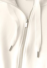 Sudadera blanca con cremallera y capucha, de textura suave, con cremallera plateada y cordones con terminales metálicos. Diseño clásico con detalles acanalados.