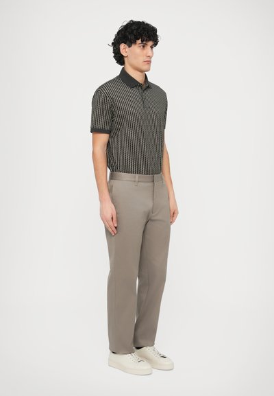 Μπλούζα πόλο κοντομάνικη με ασπρόμαυρο μοτίβο, συνδυασμένη με ανοιχτό γκρι παντελόνι και λευκά αθλητικά παπούτσια. Διαθέτει κλασικό γιακά και στενή εφαρμογή.