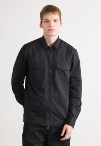 Black lightweight jacket with a front zipper, two chest pockets, and a classic collar. Smooth texture, tailored fit, and no patterns.
